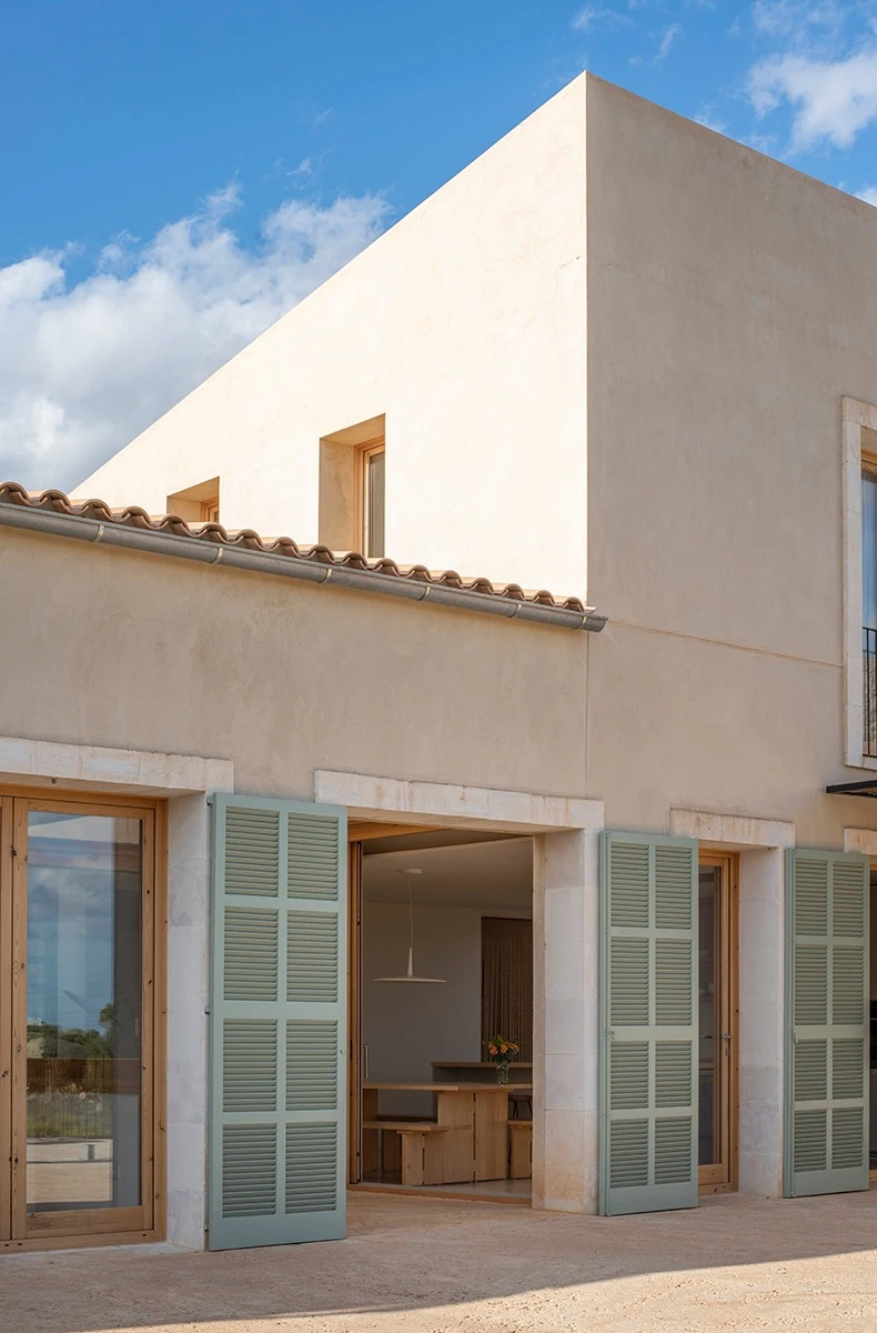 Casa LLT: volums de tons terra i persianes verdes obertes al menjador